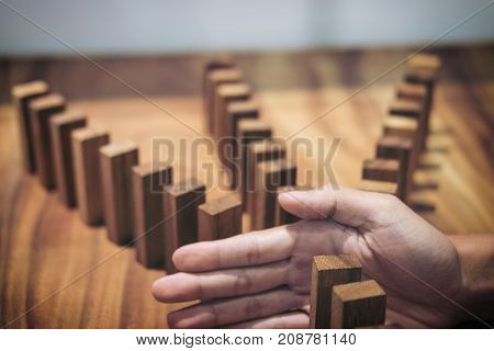 Risk and strategy in business Close up of businessman hand stopping wooden block between three way from falling in the line of domino.