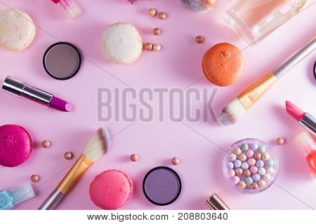 Make up products and macaroons frame on pink background