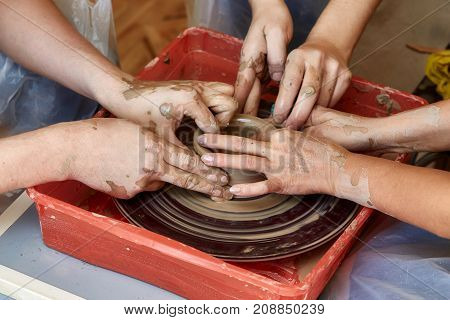 Hands of three people create pot on potter's wheel. Teaching pottery carftman's hands guiding