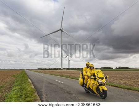 Le Gault-Saint-Denis France - October 08 2017: The iconic yellow LCL bike driving on a road in the plain with windmills in a cloudy day during the Paris-Tours road-cycling race.