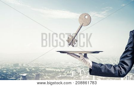 Closeup of waiter's hand in white glove presenting stone key symbol on metal tray with cityscape view on background. 3D rendering.