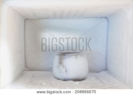 Stainless steel drinking water glass in freezer of a refrigerator. Ice buildup inside of a freezer walls.
