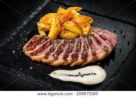 Minced meat barbecued stakes served with fried potatoes and bowls of sauces on black dish