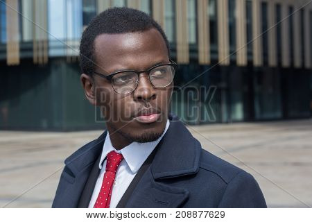 Horizontal Headshot Of Dark-skinned African Entrepreneur Standing In Street Standing Against High Bu