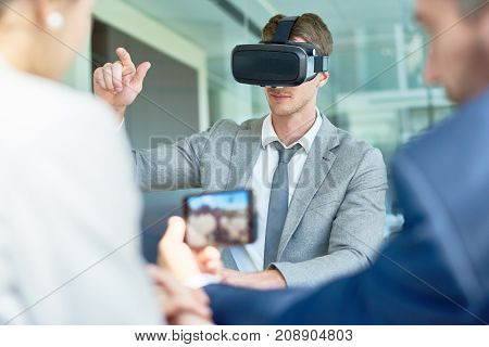 Young beaded entrepreneur using VR headset while having start-up project discussing with colleagues at spacious boardroom