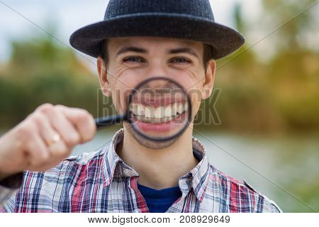 A cheerful young man with a funny face in a hat holds a magnifying glass. Let's celebrate!