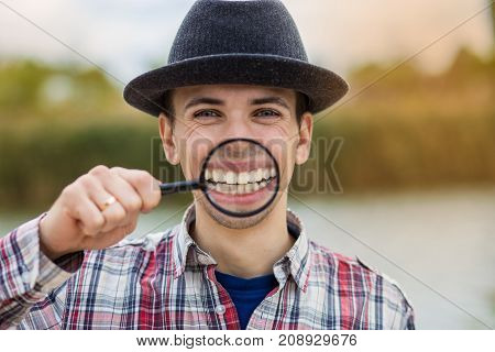 A cheerful young man with a funny face in a hat holds a magnifying glass. Let's celebrate!