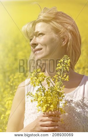 Beautiful dreamy woman in a rapeseed field with a bouquet dreams and enjoys nature