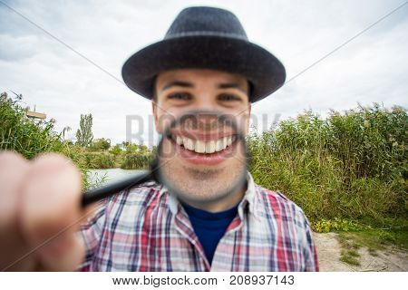 A cheerful young man with a funny face in a hat holds a magnifying glass. Let's celebrate!