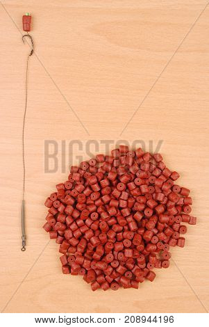 Fishing bait with hook and red pre-drilled halibut pellets for carp fishing isolated on wood background with soft shadow