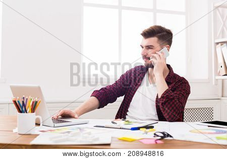 Important call. Young smiling businessman in casual talking on mobile phone in modern white office interior.