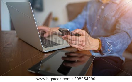 Closely modern businessman browsing wifi on mobile phone, sitting at the table with laptop computer and digital tablet. Male successful financier using for work cell telephone, net-book and touch pad