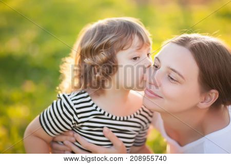 Adorable little guaghter kissing her mother. Loving daughter. Attractive youang mother. Time with parents. Caring mother happy family. Summer sunny days beautiful lightings.