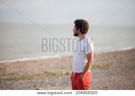 Young man standing alone on the ocean beach with calm blue sea. Lonely man concept.