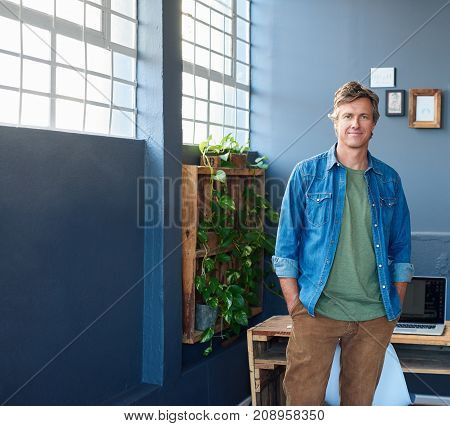 Portrait of a casually dressed business professional smiling confidently while standing with his hands in his pockets in a bright modern office