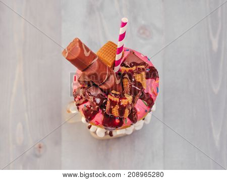 Chocolate and donuts extreme milkshake with marshmallow and other sweets in mason jar on gray wooden background. Crazy freakshake on gray wooden table with copy space