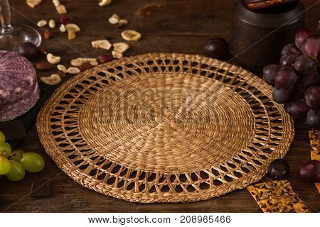 Food background of gourmet products. Void straw mat with quality sort of cheese and assortment of appetizers, close up