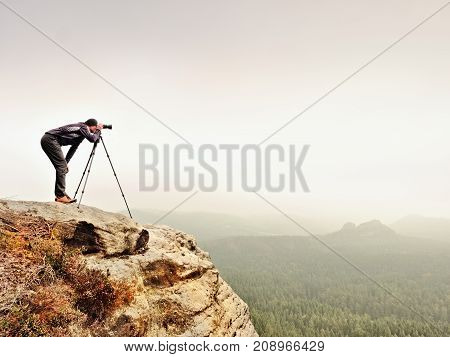 Hiker With Camera On Tripod Takes Picture From Rocky Summit. Alone Photographer  On Summit