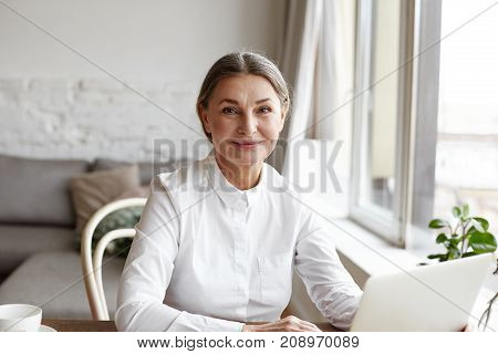 Portrait of happy skilled middle aged woman life coach business consultant psychologist or medical advisor smiling joyfully at camera working on laptop enjoying her job helping people online