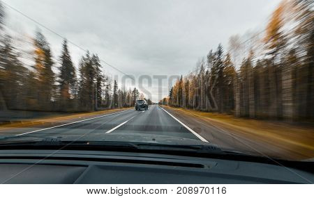Autumn forest road at high speed drive. View from windscreen. Crossover car overtakes us.