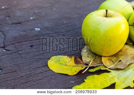 Ripe green apples on a wooden background with yellow leaves.