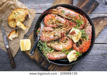 Traditional fried black tiger prawn with garlic bread as top view in a black frying pan 