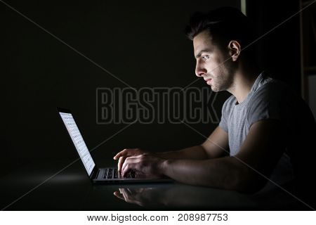 Young Man Reading News On Laptop Lying In Dark Room. Looking Concentrated