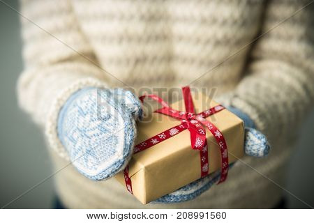 Christmas background. A girl in a warm knitted sweater and mittens is holding a Christmas present. Gifts for men. Merry Christmas. Gift for a girl. Knitted mittens. Knitted dress. Box with gifts.