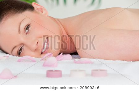 Sorrindo Youn mulher mentir sobre sua barriga com pétalas e velas Unlighted