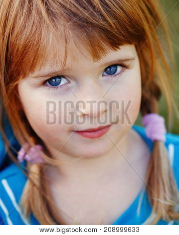 Closeup portrait of cute adorable little red-haired Caucasian girl child with blue eyes looking in camera. Happy childhood concept