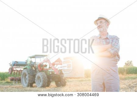 Senior farmer standing at fielf against tractor