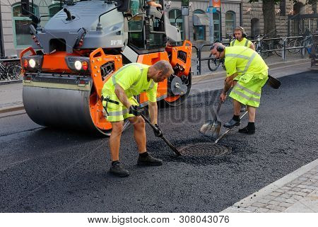 Karlstad, Sweden - June 19, 2019: Road Workers Asphalting Manualy The Area Around A Manhole.
