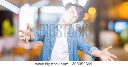 Young handsome man wearing glasses over isolated background looking at the camera smiling with open arms for hug. Cheerful expression embracing happiness.