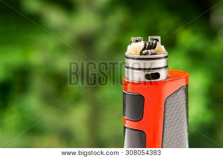 Electronic Cigarette On The Background Of Trees, Visible Spiral Wool And Steam. Coil Cleaning.