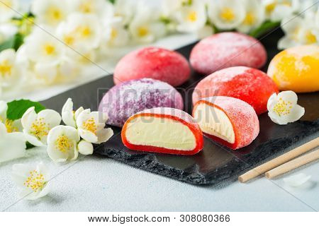 Multi-colored Japanese Ice Cream Mochi In Rice Dough And Jasmine Flowers On A Concrete Blue Backgrou