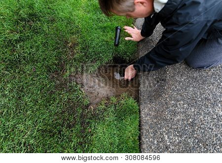 Sprinkler System Being Repaired By Mature Man With Parts Laying On Ground