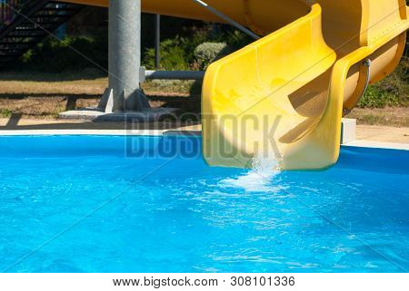 Yellow Water Slide With Blue Swimming Pool In Aqua Amusement Park During Summer Sunny Day