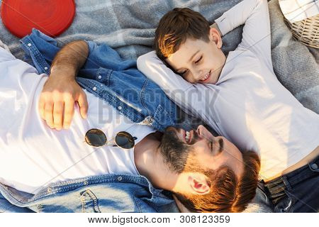 Image of a happy young man having fun with his little brother or son outoors in park lies.