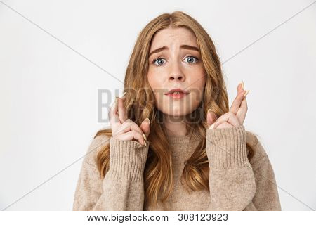 Attractive young girl wearing sweater standing isolated over white background, holding fingers crossed for good luck