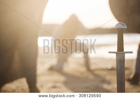 Sword At Buttlefield And Defeated Warriors, Reencators With Wearpons At Seaside