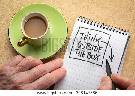 Think outsite the box man hand writing a note with a black marker in a spiral notebook