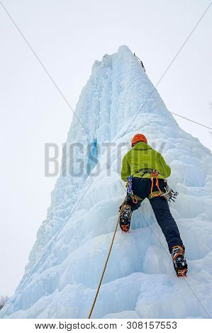 Alpinist Man With Ice Tools Axe In Orange Helmet Climbing A Lar
