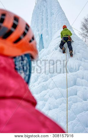 Alpinist Man With Ice Tools Axe In Orange Helmet Climbing A Lar