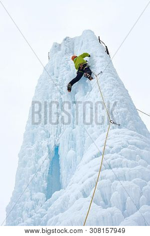 Alpinist Man With Ice Tools Axe In Orange Helmet Climbing A Lar