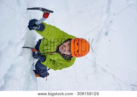 Alpinist Man With Ice Tools Axe In Orange Helmet Climbing A Lar