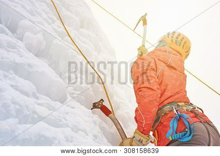 Alpinist Woman With Ice Tools Axe In Orange Helmet Climbing A L