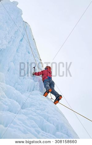 Alpinist Woman With Ice Tools Axe In Orange Helmet Climbing A L