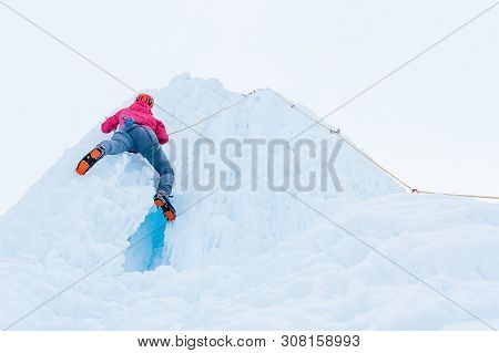 Alpinist Woman With Ice Tools Axe In Orange Helmet Climbing A Large Wall Of Ice. Outdoor Sports Port