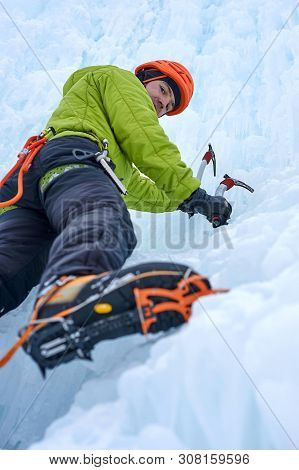Alpinist Man With Ice Tools Axe In Orange Helmet Climbing A Lar