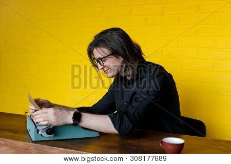 Profile Of A Amusing Man In Black Clothing Inserting New Paper Into Typewriter, Over Yellow Backgrou